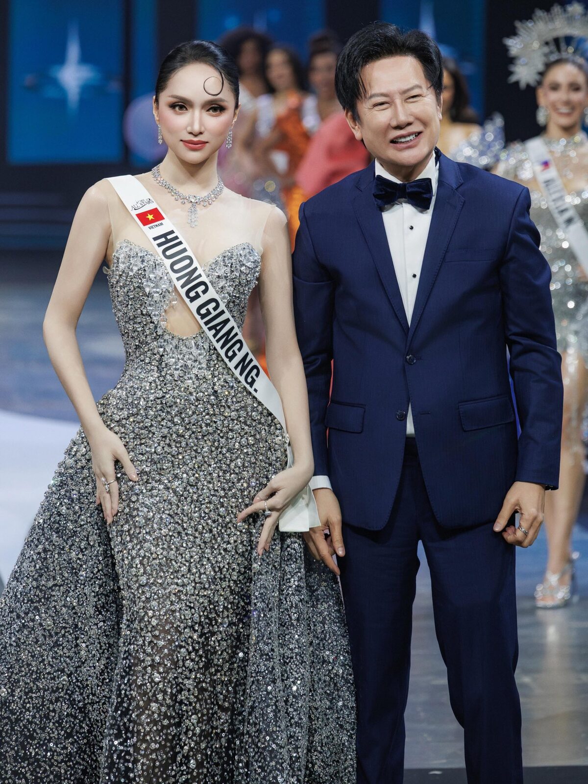 Ngày 19/5, Hương Giang nhận sash (dải băng đeo cho thí sinh) từ ông Nawat (phải) - chủ tịch cuộc thi. Trong khuôn khổ sự kiện, cô được ban tổ chức dành cho màn catwalk riêng vì dẫn đầu hạng mục bình chọn All Stars: World Famous.
