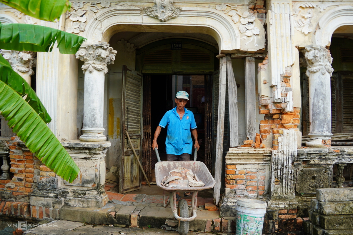 Công nhân vận chuyển các viên gạch vỡ từ nóc nhà. Một bên cửa chính của căn nhà cổ cột đã gãy mất, tường, gạch vỡ vụn, chủ nhà phải dùng thanh gỗ chống đỡ tạm.