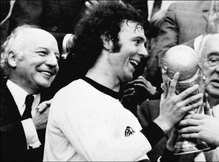 5. Franz Beckenbauer (Đức) Cựu danh thủ Glenn Hoddle từng nói dấu hiệu của một cầu thủ vĩ đại là khả năng tỏa sáng ở những thời kỳ khác nhau của bóng đá. Franz Beckenbauer là ví dụ tiêu biểu. Ông dự ba kỳ World Cup liên tiếp trong giai đoạn bóng đá thế giới thay đổi mạnh mẽ về chiến thuật và luôn nằm ở trung tâm của những thay đổi đó. Beckenbauer khởi nghiệp ở hàng tiền vệ trước khi được kéo xuống hàng thủ. Dù không phải người phát minh vai trò libero (hậu vệ quét), ông được xem là người hoàn thiện vị trí này. Tại World Cup 1966, Beckenbauer ghi bốn bàn, góp công lớn giúp Tây Đức vào chung kết. Bốn năm sau ở Mexico, ông tiếp tục ghi dấu ấn trong chiến thắng nổi tiếng trước Anh. Tuy nhiên, hình ảnh được nhớ đến nhiều nhất là ở bán kết World Cup 1970 gặp Italy, trong "Trận cầu thế kỷ". Sau khi bị trật khớp vai, Beckenbauer vẫn thi đấu đến hết trận với cánh tay được cố định bằng dây đeo vì Tây Đức đã sử dụng hết quyền thay người. Đến World Cup 1974, ông hoàn tất bộ sưu tập khi cùng Tây Đức đánh bại Hà Lan 2-1 trong trận chung kết trên sân nhà. Dù nhiều CĐV trung lập tiếc nuối cho Johan Cruyff và "Bóng đá tổng lực" của Hà Lan, ít ai phủ nhận Beckenbauer xứng đáng nâng cao chiếc Cup vàng.