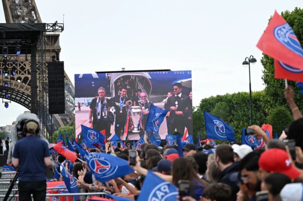 Người hâm mộ PSG cổ vũ trước màn hình lớn hiển thị hình ảnh HLV Luis Enrique cùng các cầu thủ khi đội bóng hạ cánh xuống Paris trong lễ mừng chức vô địch Champions League, dưới chân tháp Eiffel, ngày 31/5/2026. Ảnh: AP