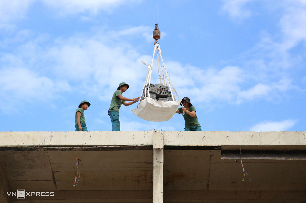 Giữa trưa nắng, dân quân tự vệ đứng trên tầng 4 chờ máy cẩu đưa gạch lên cao rồi nhanh chóng vận chuyển đến vị trí thi công.