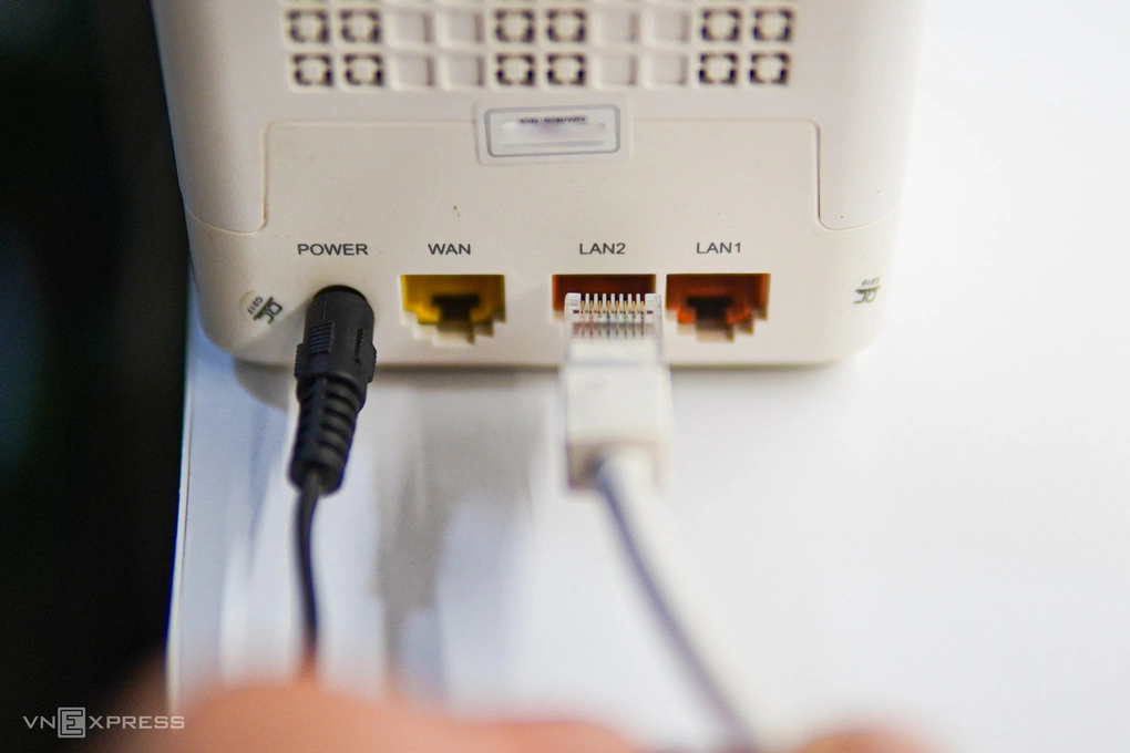 Hình ảnh cận cảnh tay người đang cắm cáp Ethernet vào cổng LAN của modem/router Wi-Fi kết nối Internet. Ảnh: Lưu Quý